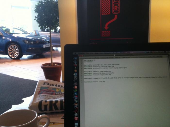 Working on a laptop with new cars on the showroom floor behind