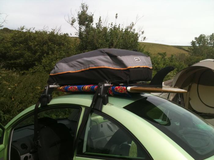 VW Beetle with a roof box and surfboard at a campsite