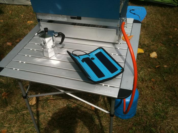 Blue folding solar charger on a camping table next to a coffee pot