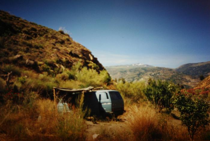 Blue T25 panel van under a makeshift shelter on a hillside