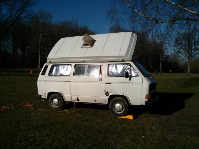 T25 camper with the pop top raised in a forest clearing