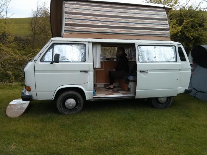 T25 with the pop top up and the side door open at a campsite