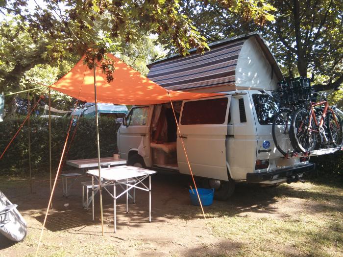 T25 camper with an orange canopy at a campsite