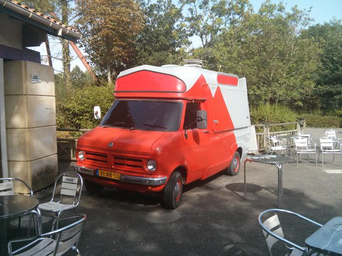 Red and white Bedford camper van parked by a cafe terrace