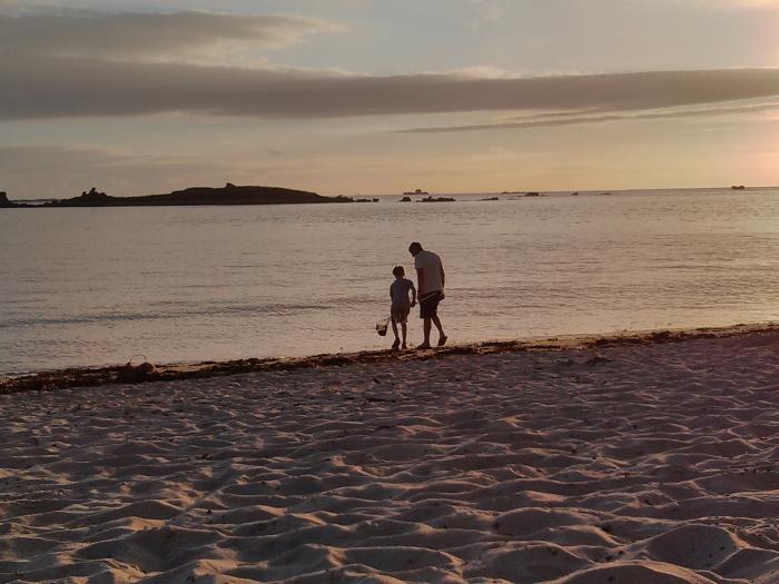 Adult and child walking on a beach at sunset