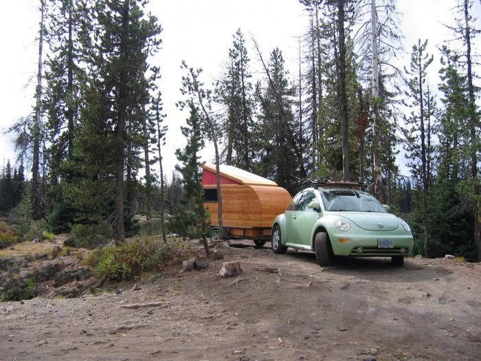 VW Beetle towing a small wooden trailer in a forest